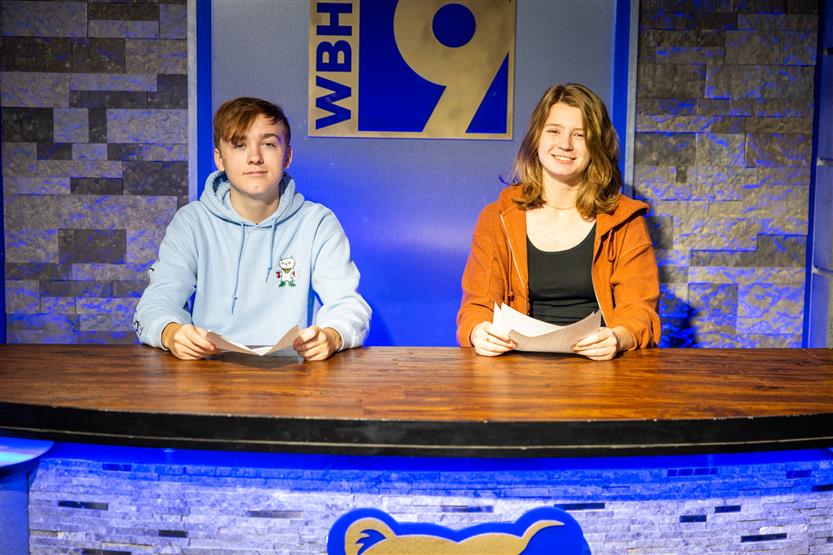 Two students sit at a news desk